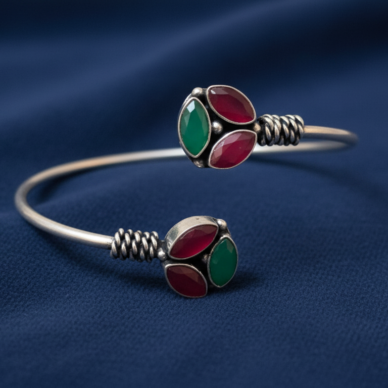 Silver bracelet with red and green gemstones on a blue fabric background