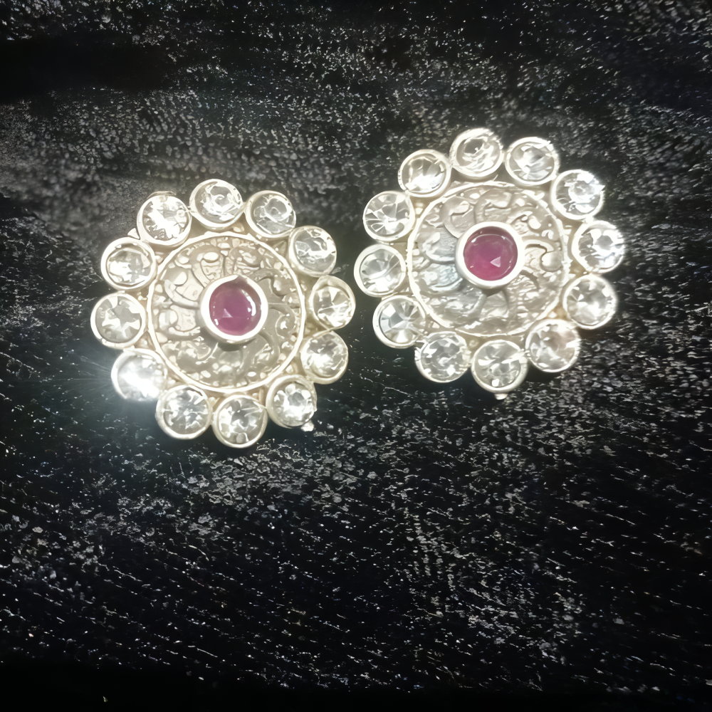 Pair of silver ornate earrings with pink at the centre & clear kundan stones all around.