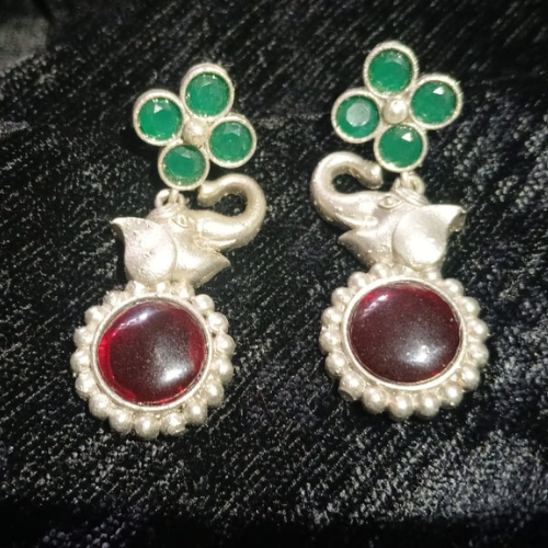 Elephant earrings with green gemstones and red stones on a black textured background .