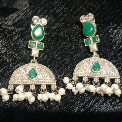 Oxidised silver earrings with green stones and pearl-like beads on a black background .