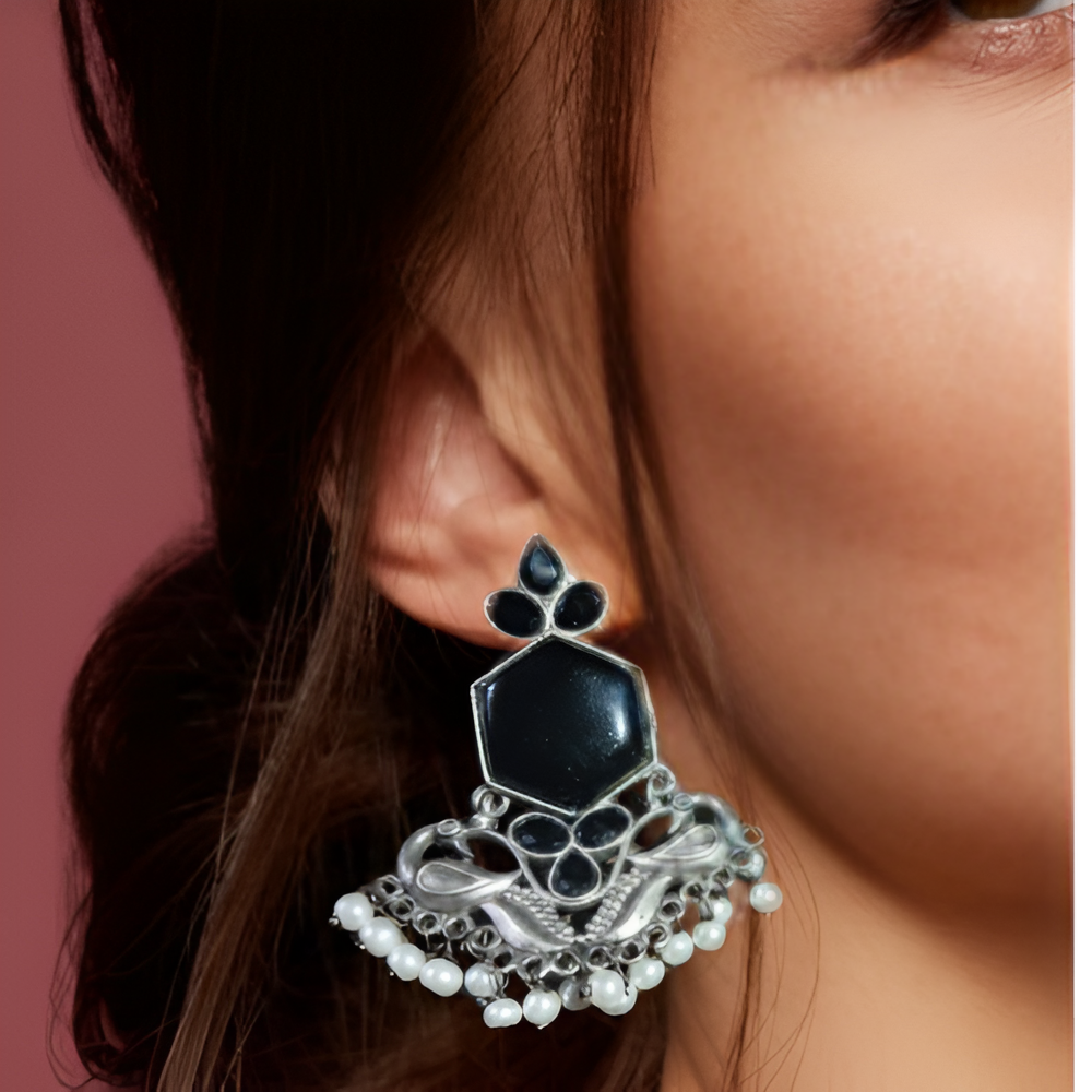 A lady wearing an oxidised earring with a black gemstone and pearl details.