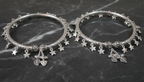 Two silver bangles with star and leaf charms on a dark marble surface