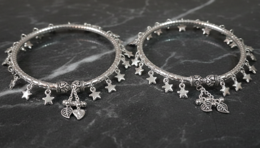 Two silver bangles with star and leaf charms on a dark marble surface