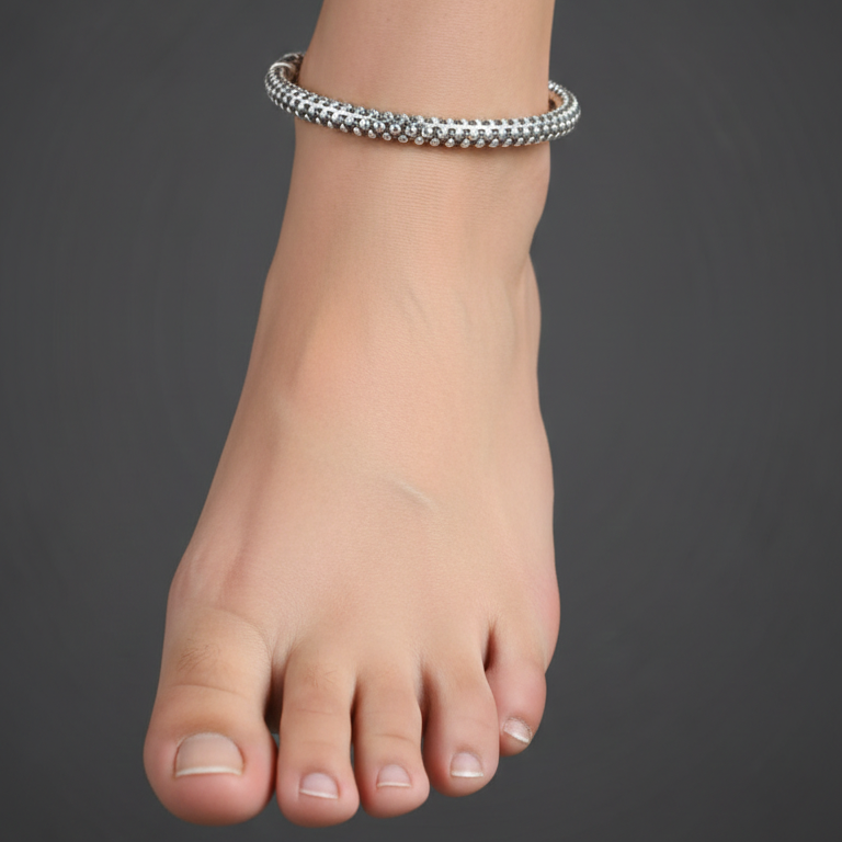 Silver anklet on a foot against a dark background