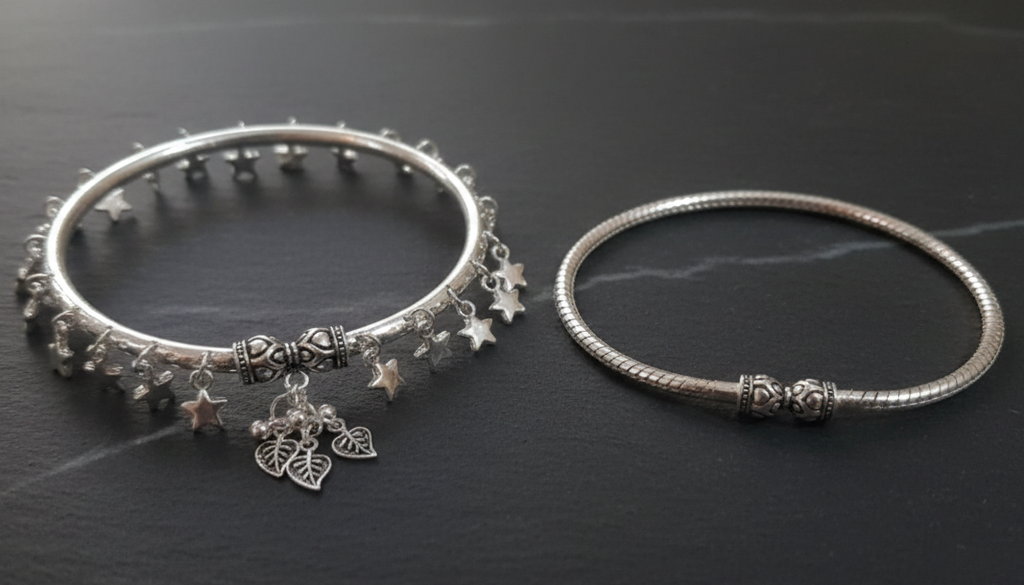 Two silver ankle bracelets on a dark surface