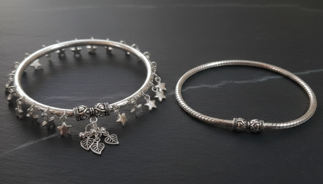 Two silver ankle bracelets on a dark surface