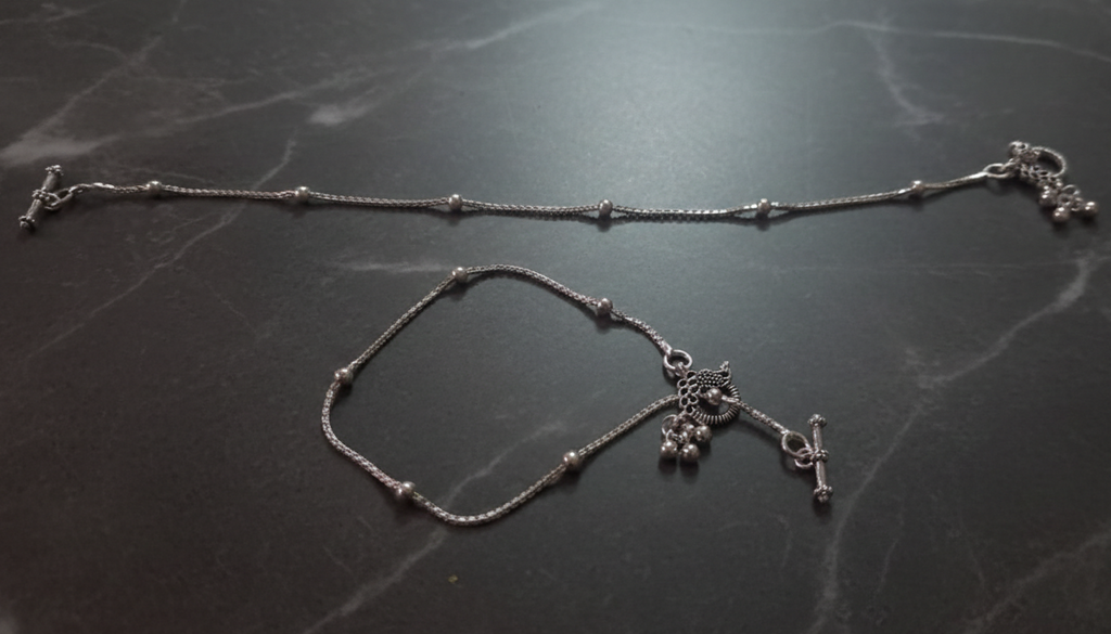 Silver anklet with charms on a dark marble surface