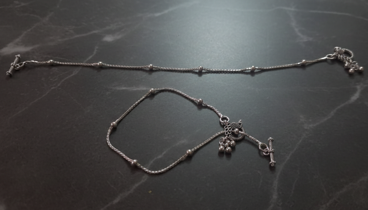 Silver anklet with charms on a dark marble surface