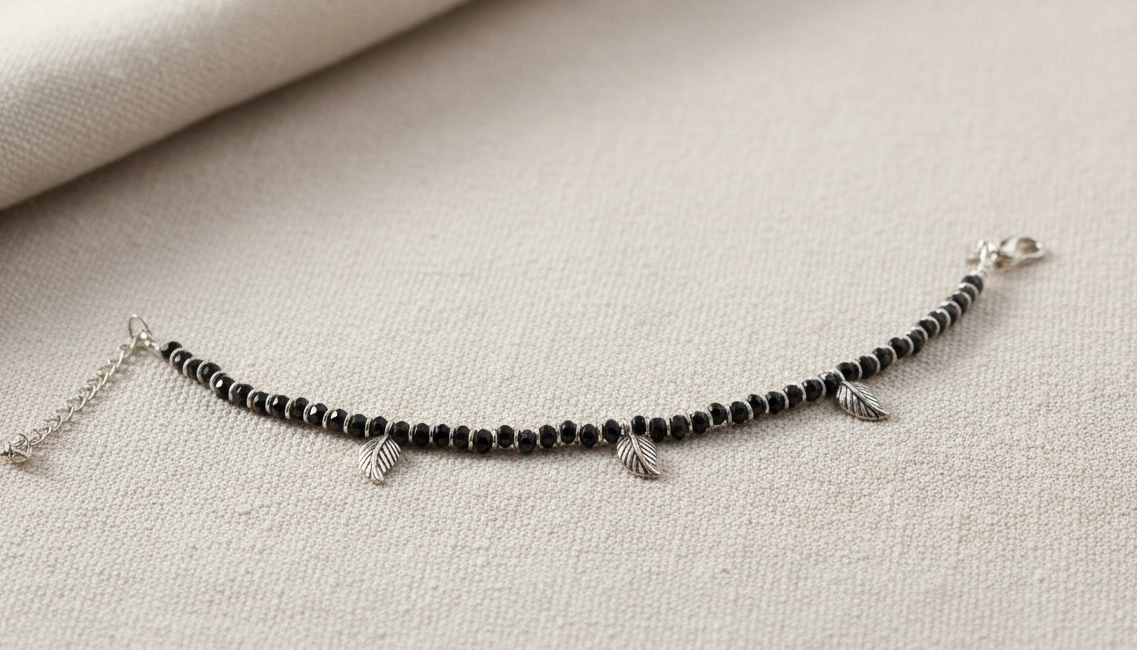 Black beaded bracelet with silver charms on a beige fabric background