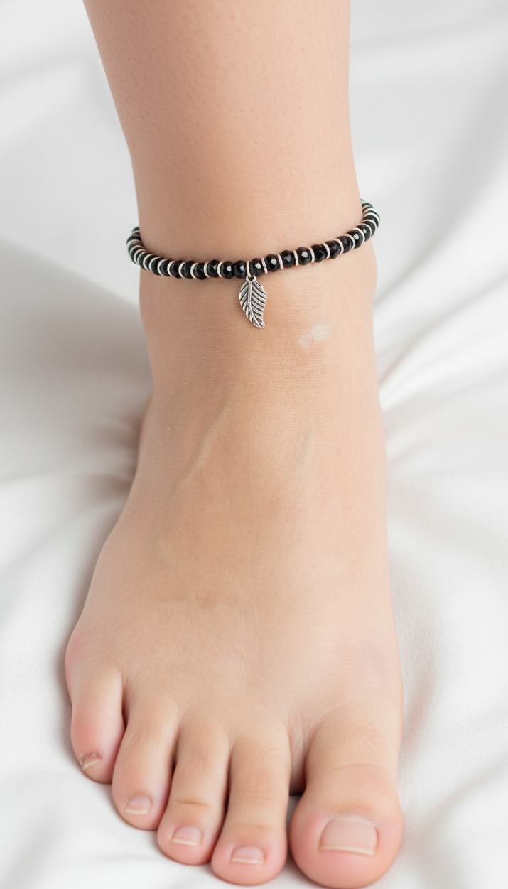 Ankle with black beaded bracelet featuring a silver leaf charm on a white background