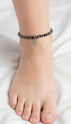 Ankle with black beaded bracelet featuring a silver leaf charm on a white background