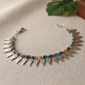 Anklet bracelet with leaf-shaped pendants and colorful beads on a textured surface