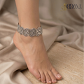 Silver anklet with carvingon a foot with a beige fabric background