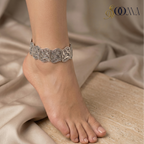 Silver anklet with carvingon a foot with a beige fabric background