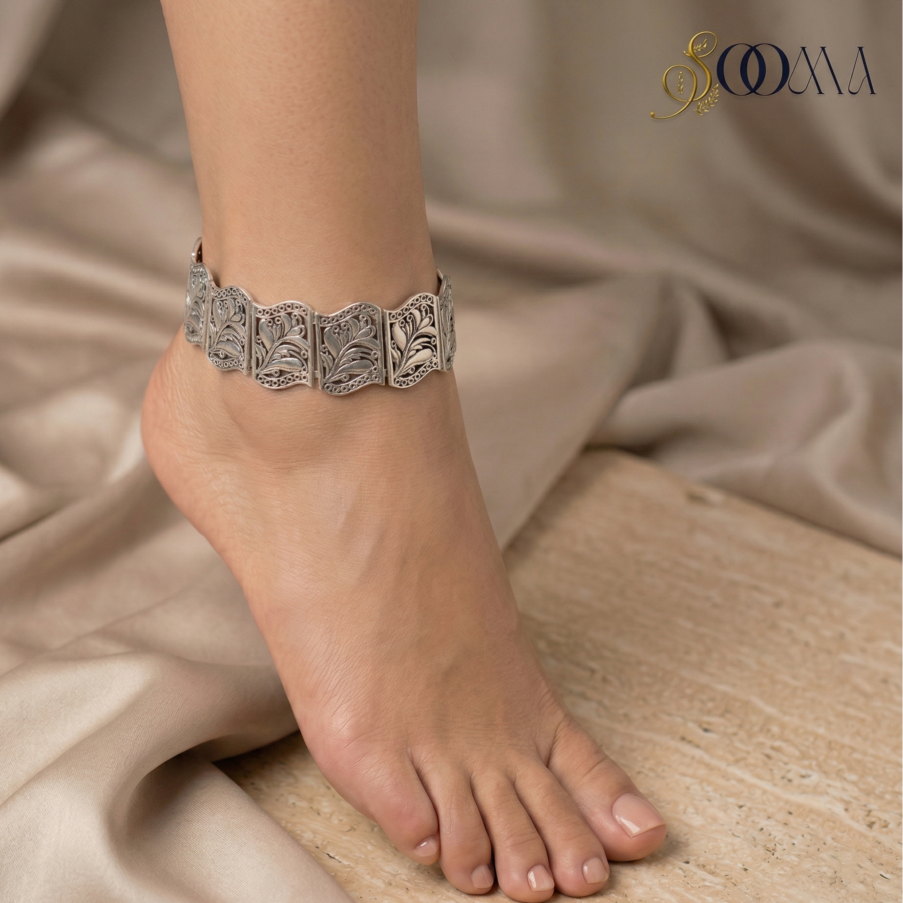Silver anklet with carvingon a foot with a beige fabric background