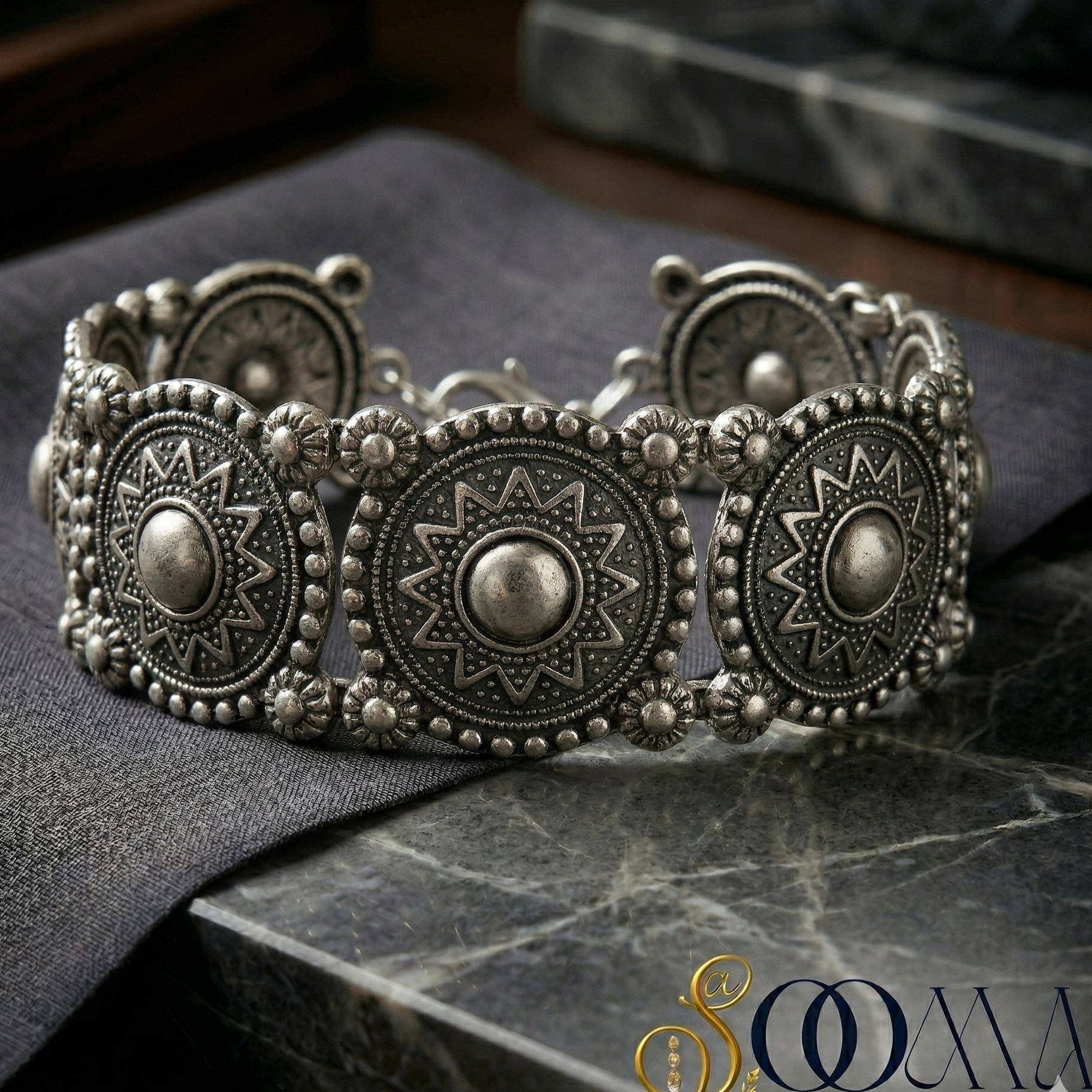 Decorative silver ankle bracelet on a dark fabric surface with a blurred background