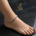 Ankle bracelet on a foot with a dark background and 'Sooma' branding.