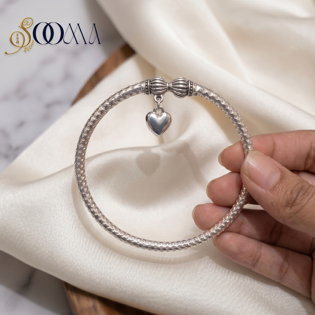 Silver bracelet with a heart charm held by a hand on a white fabric background