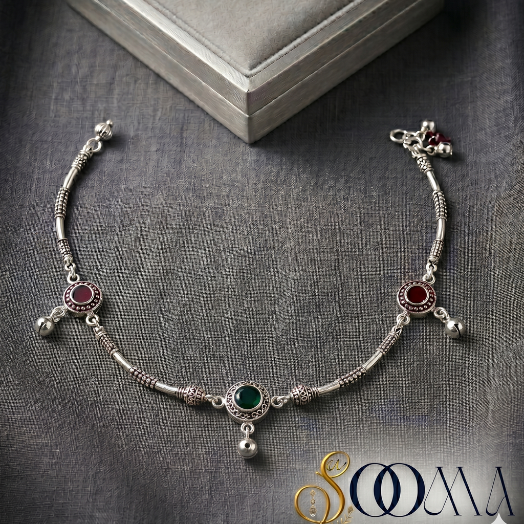 Silver anklet with gemstones on a gray fabric background, featuring the brand 'Sooma'.