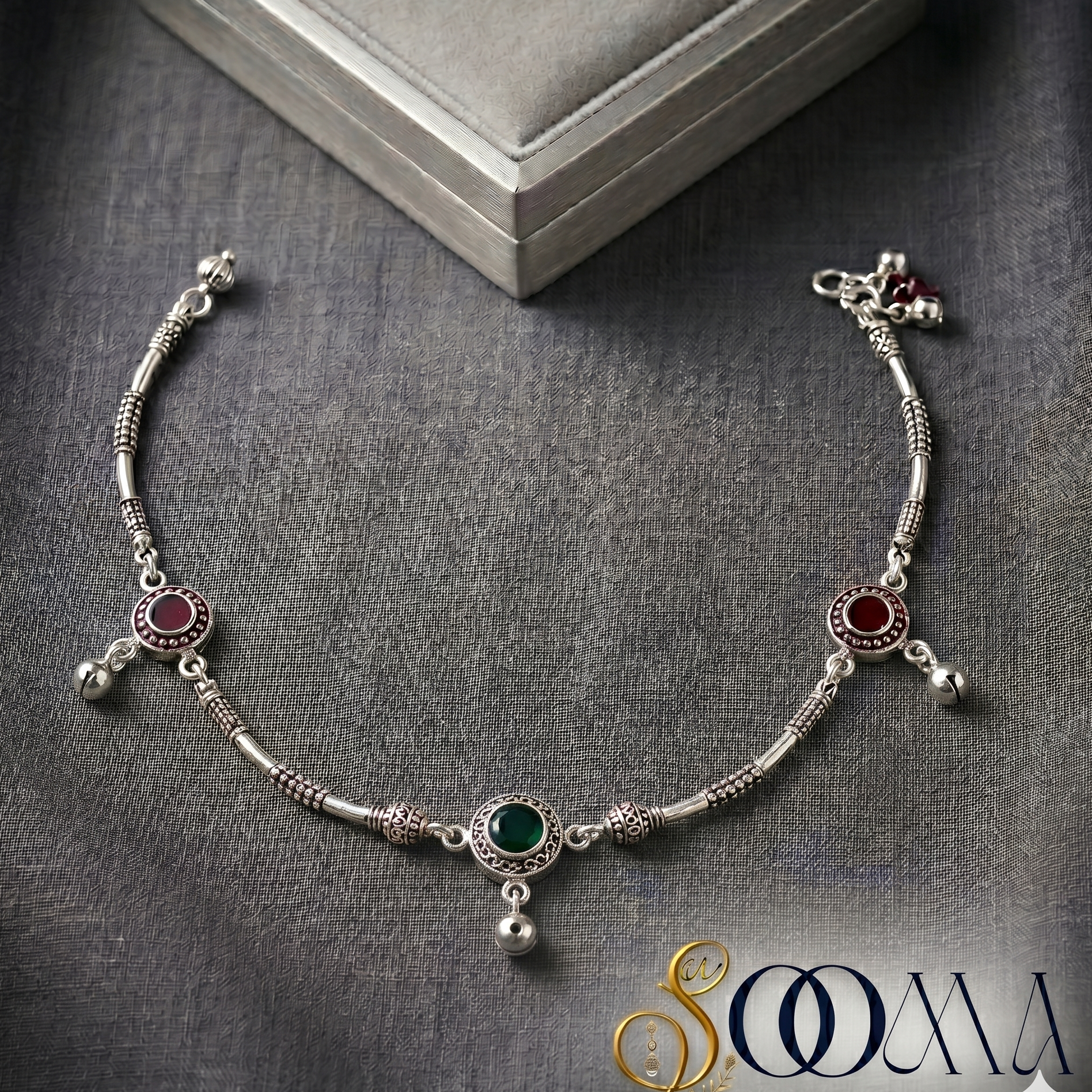 Silver anklet with gemstones on a gray fabric background, featuring the brand 'Sooma'.