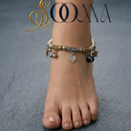 Ankle with multiple bracelets on a gray textured background, featuring the brand 'Sooma'.