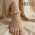 Gold anklet on a foot with 'Sooma' branding against a beige fabric background