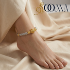 Gold anklet on a foot with a soft beige fabric background, featuring the brand 'Sooma'.