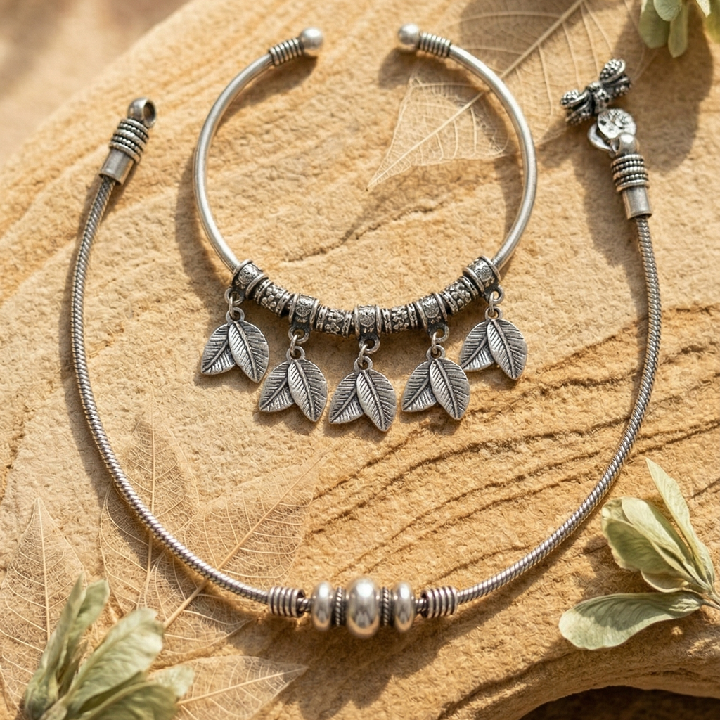 Silver anklet kada with leaf charms & silver beaded anklet on a wooden surface.