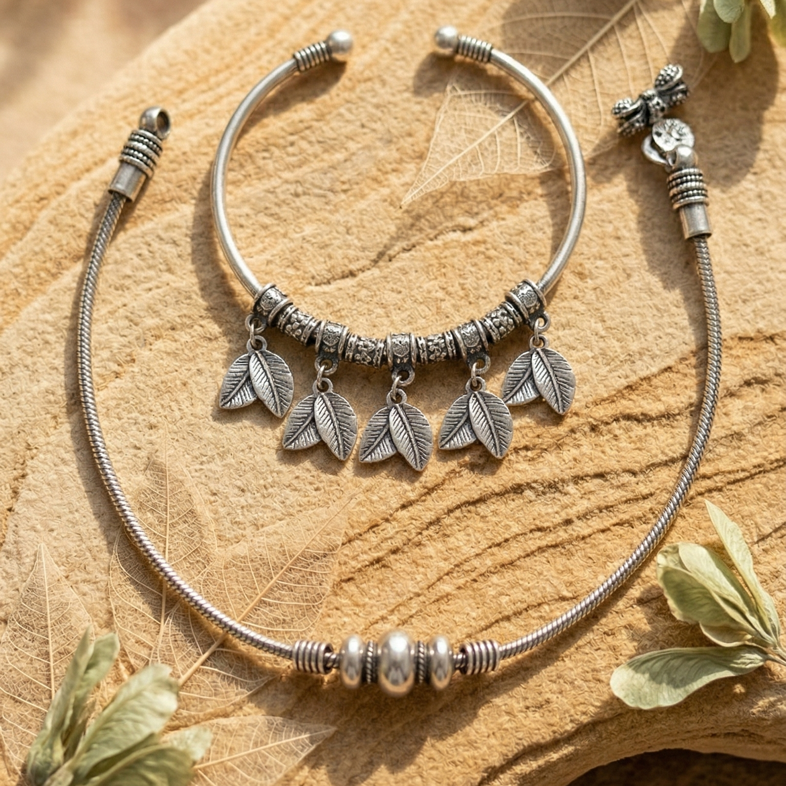 Silver anklet kada with leaf charms & silver beaded anklet on a wooden surface.