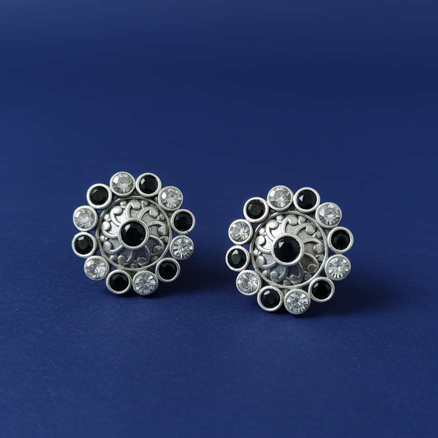 Pair of silver earrings with black and clear gemstones on a blue background