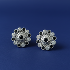 Pair of silver earrings with black and clear gemstones on a blue background