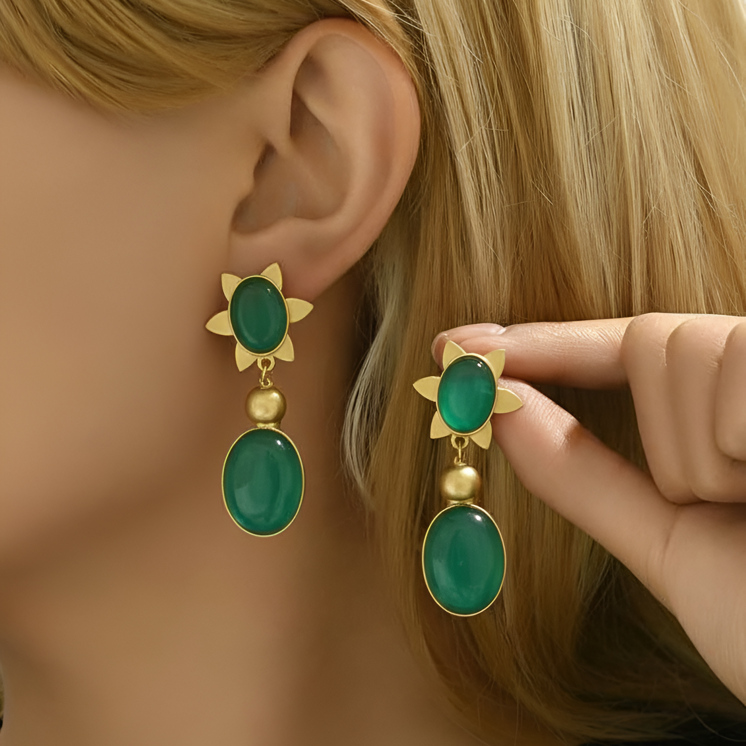 Green earrings with gold accents being worn on a mannequin ear.