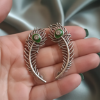Close-up of a handcrafted peacock earcuff showcasing intricate details and shimmering stones.