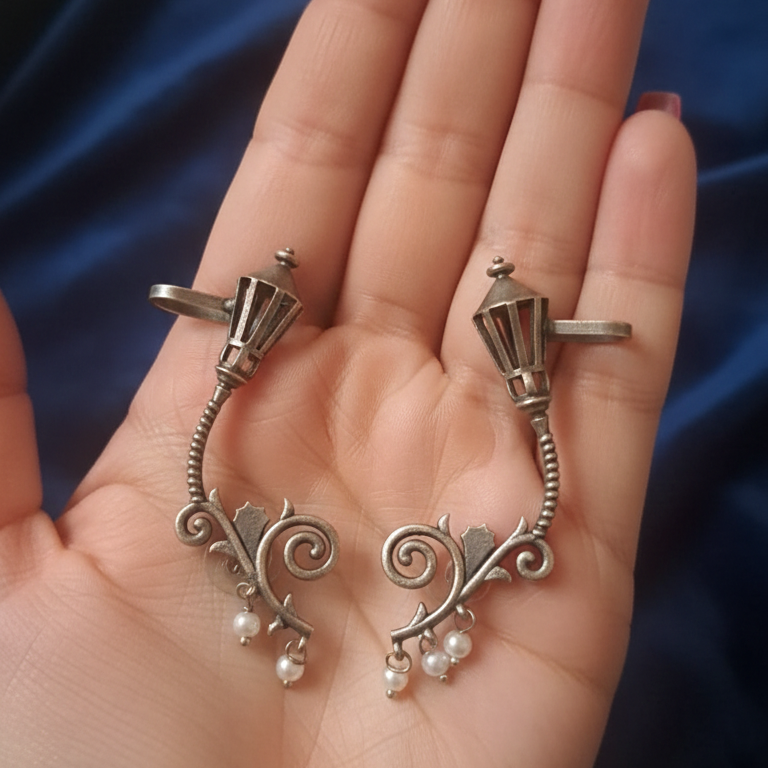 Silver ear cuff with pearl accents held in a hand against a dark blue fabric background