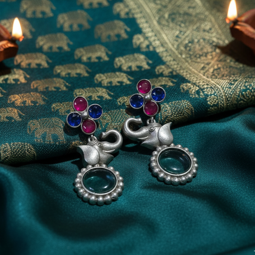 Silver elephant earrings with colorful stones on a green fabric background
