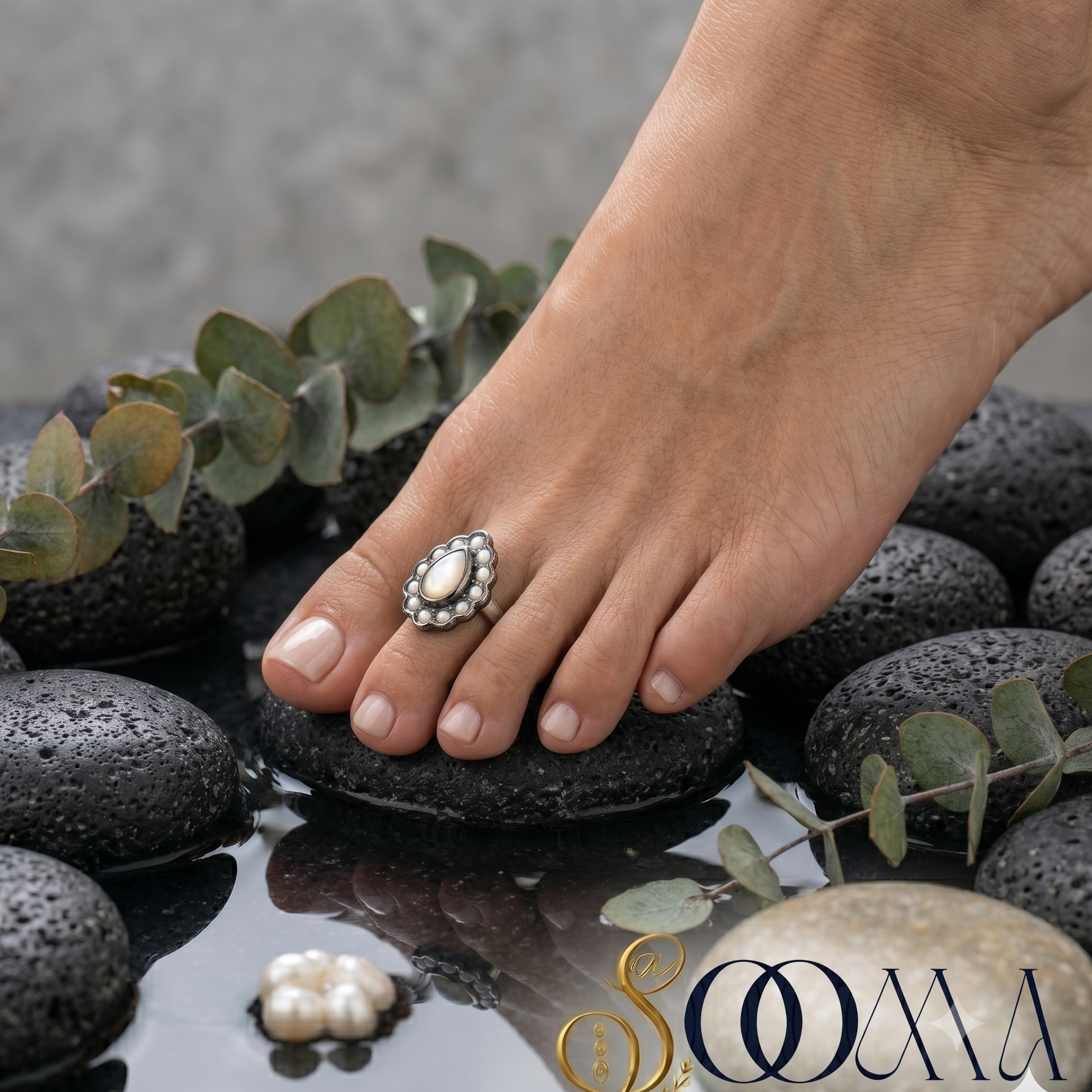 Side profile of a model's foot wearing an adjustable silver teardrop mother of pearl toe ring on a black river rock over reflective water