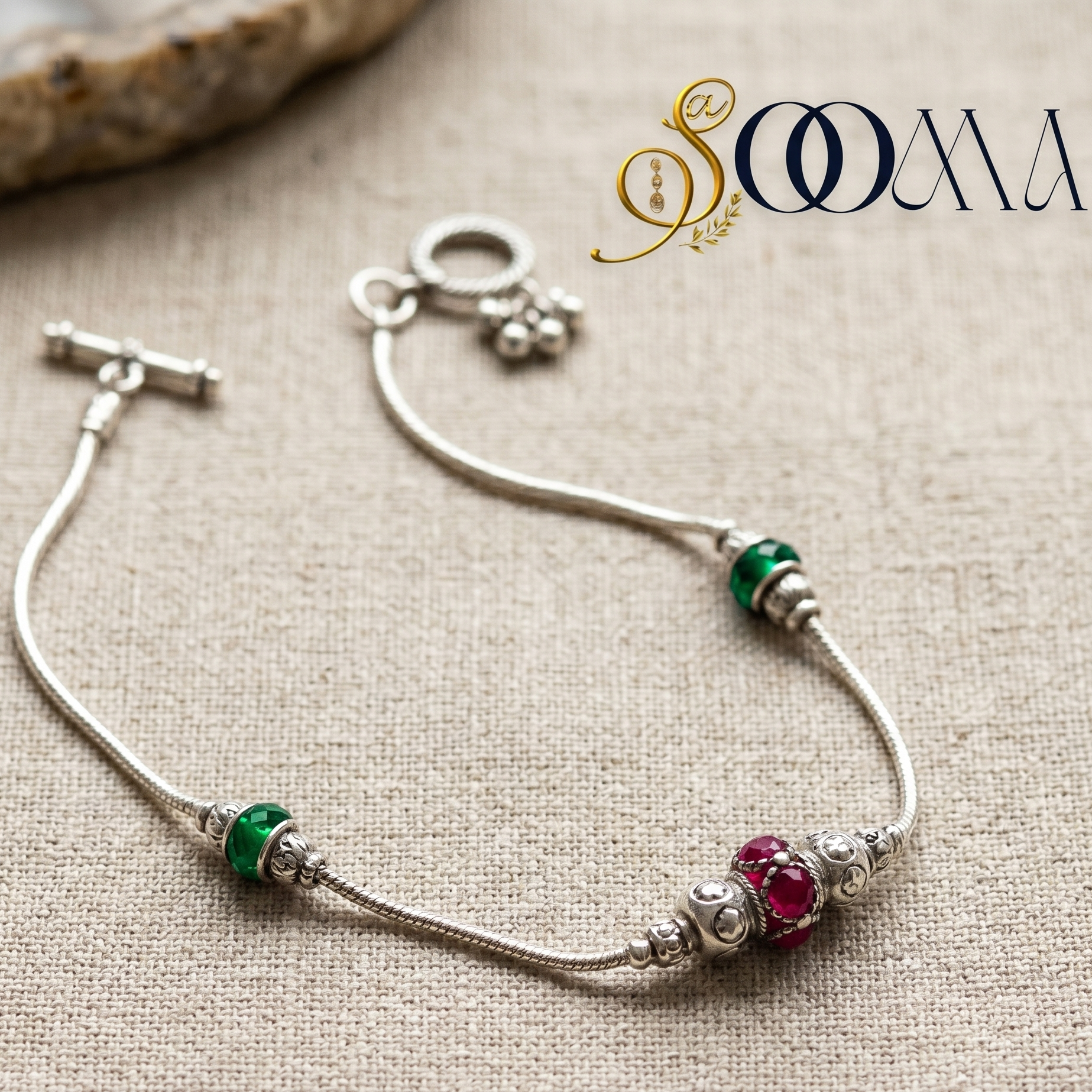 Silver ankle bracelet with colored beads on a textured beige surface, featuring the brand 'Sooma'.