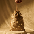 Hand holding a small brown drawstring bag with pearl-like beads against a warm-toned background