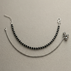 Anklets with black beads and silver chain on a beige background