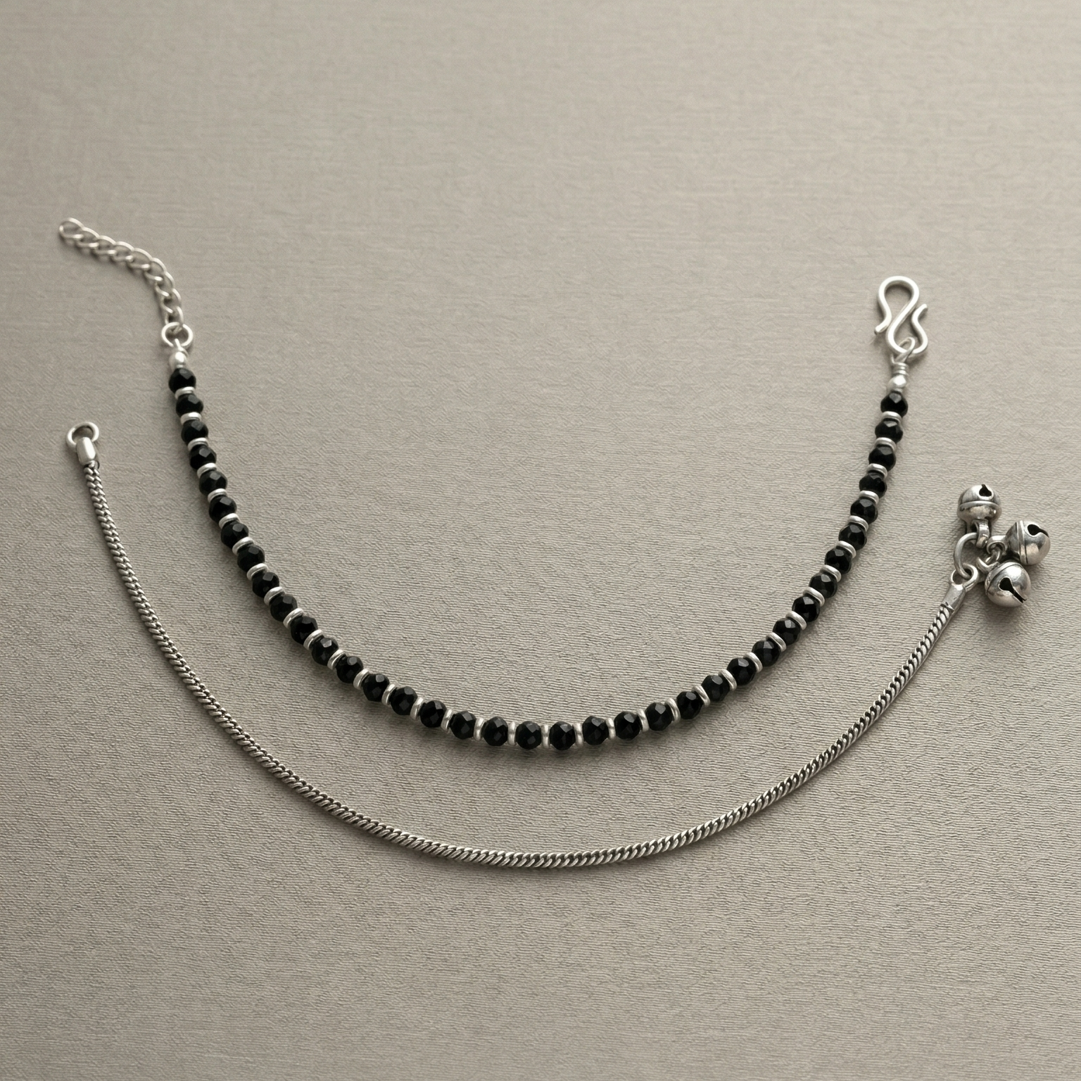 Anklets with black beads and silver chain on a beige background