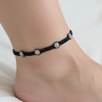 Black anklet with floral charms on a person's ankle against a white background