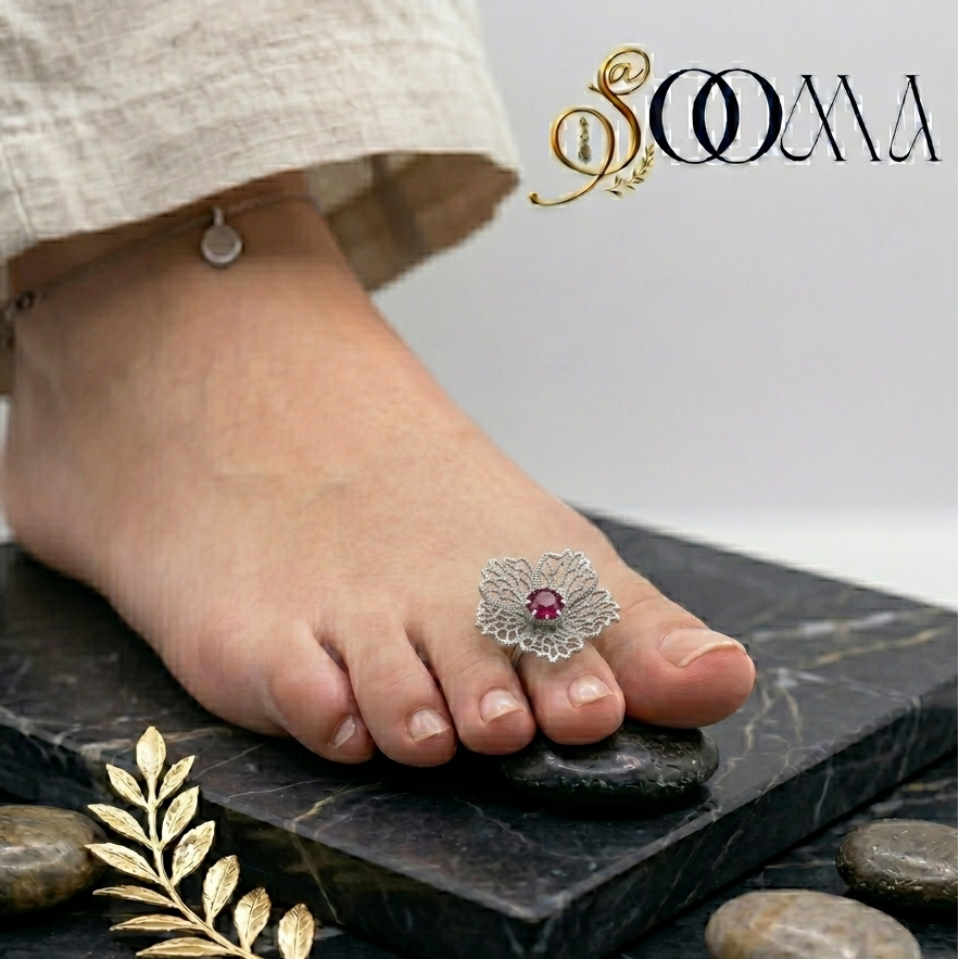 Side profile view of a model wearing a large silver filigree floral toe ring with a red gemstone on a dark marble slab with an ankle chain