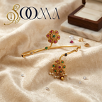 A pair of gold-toned traditional Indian bangles with intricate floral and paisley motifs, embellished with red, green, and blue stones and small pearl-like beads, displayed on draped beige fabric with a jewelry box in the background.