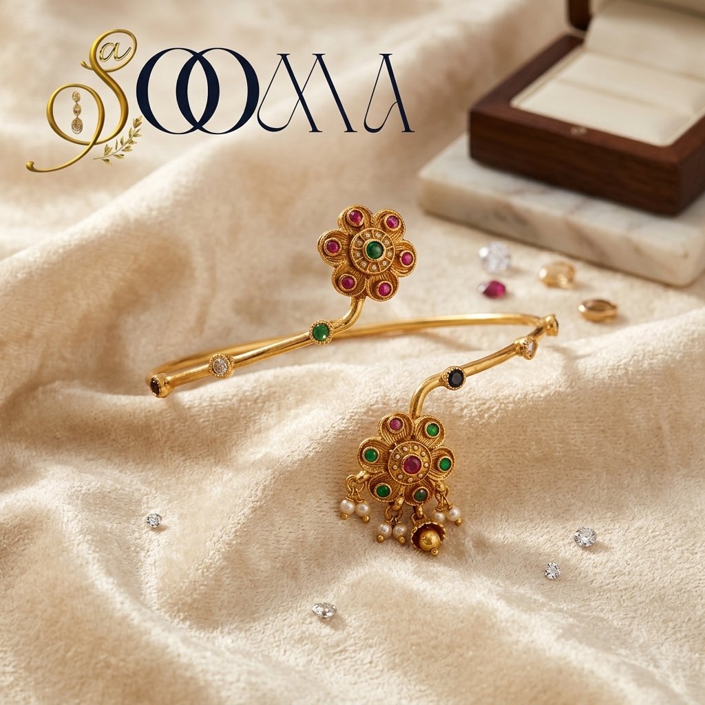 A pair of gold-toned traditional Indian bangles with intricate floral and paisley motifs, embellished with red, green, and blue stones and small pearl-like beads, displayed on draped beige fabric with a jewelry box in the background.
