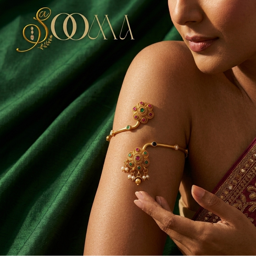 A woman wearing a gold-toned traditional Indian arm bracelet (kara) with green and red stones and pearl beads, set against a dark green draped fabric background with the brand name 'SOMA' in gold.