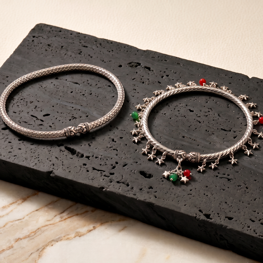 Two silver anklets with star and heart charms on a black stone surface.