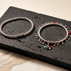 Two silver anklets with star and heart charms on a black stone surface.