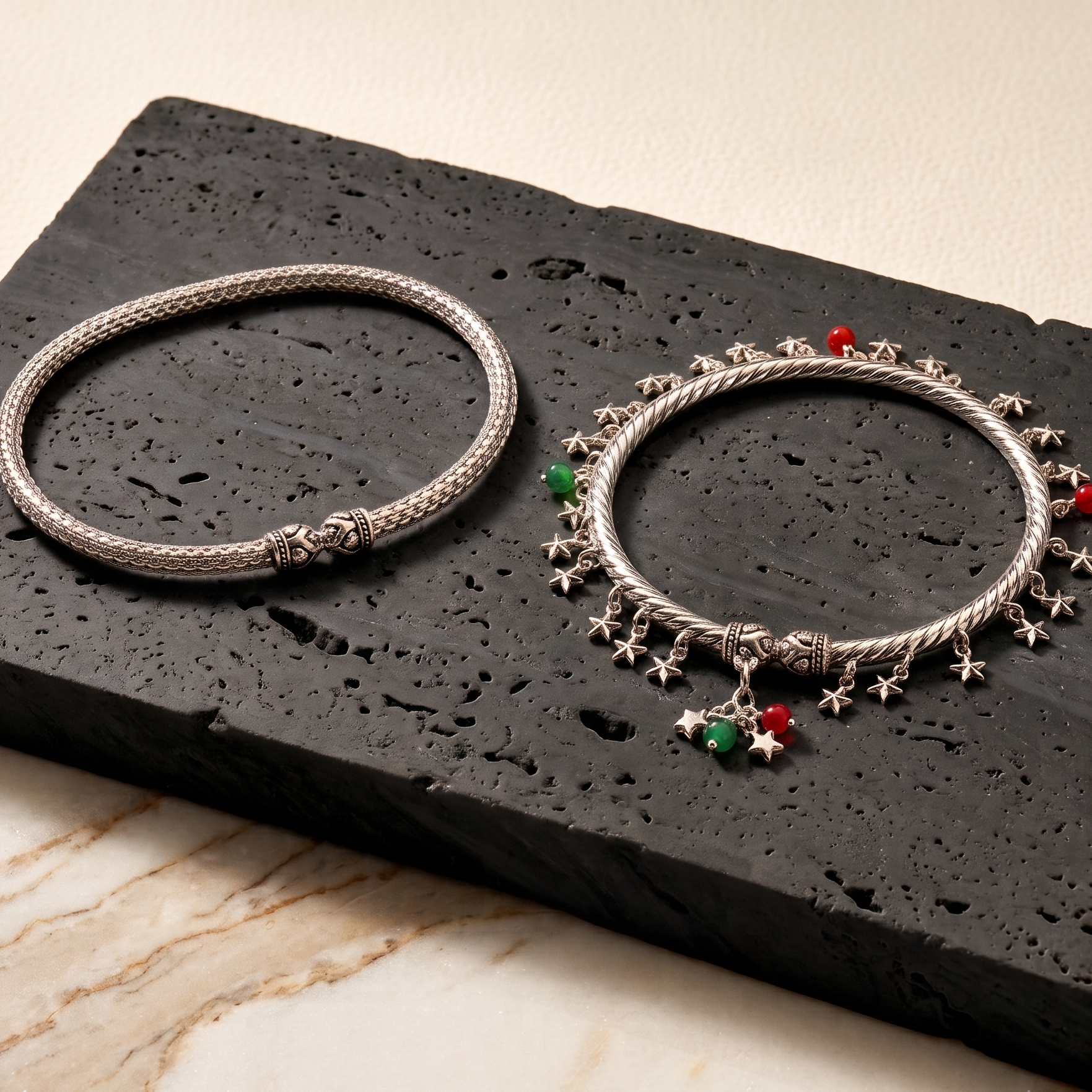 Two silver anklets with star and heart charms on a black stone surface.