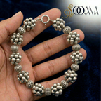 Silver beaded ankle bracelet on a hand with a dark textured background
