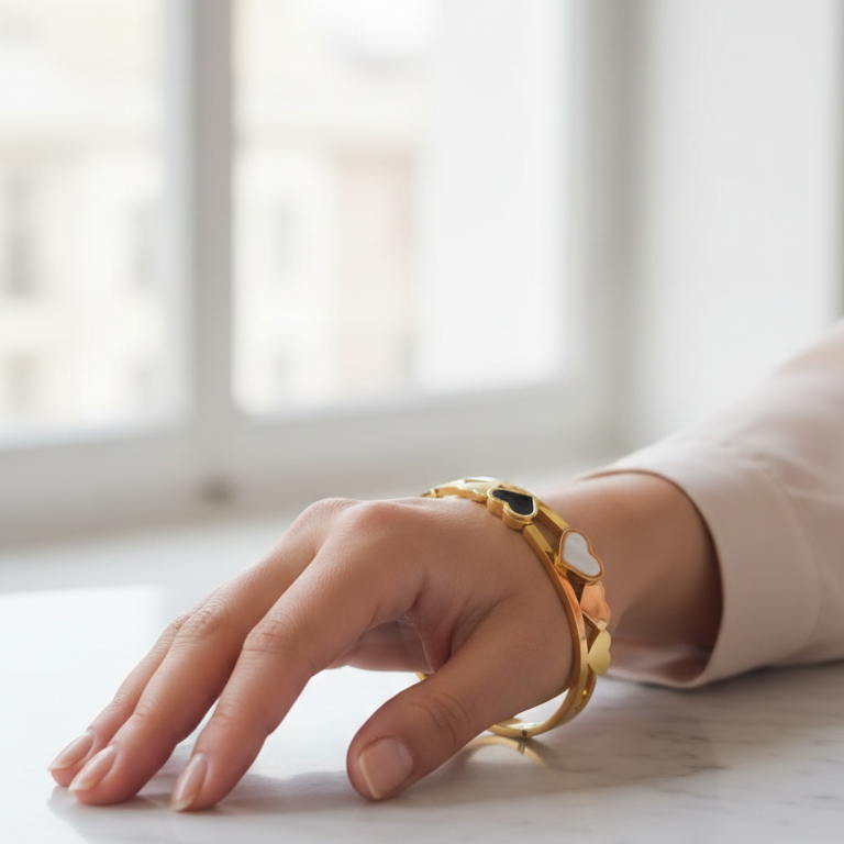 Hand wearing a gold heart bracelet on a marble surface 